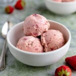 Three scoops of roasted strawberry ice cream in a small white ceramic bowl