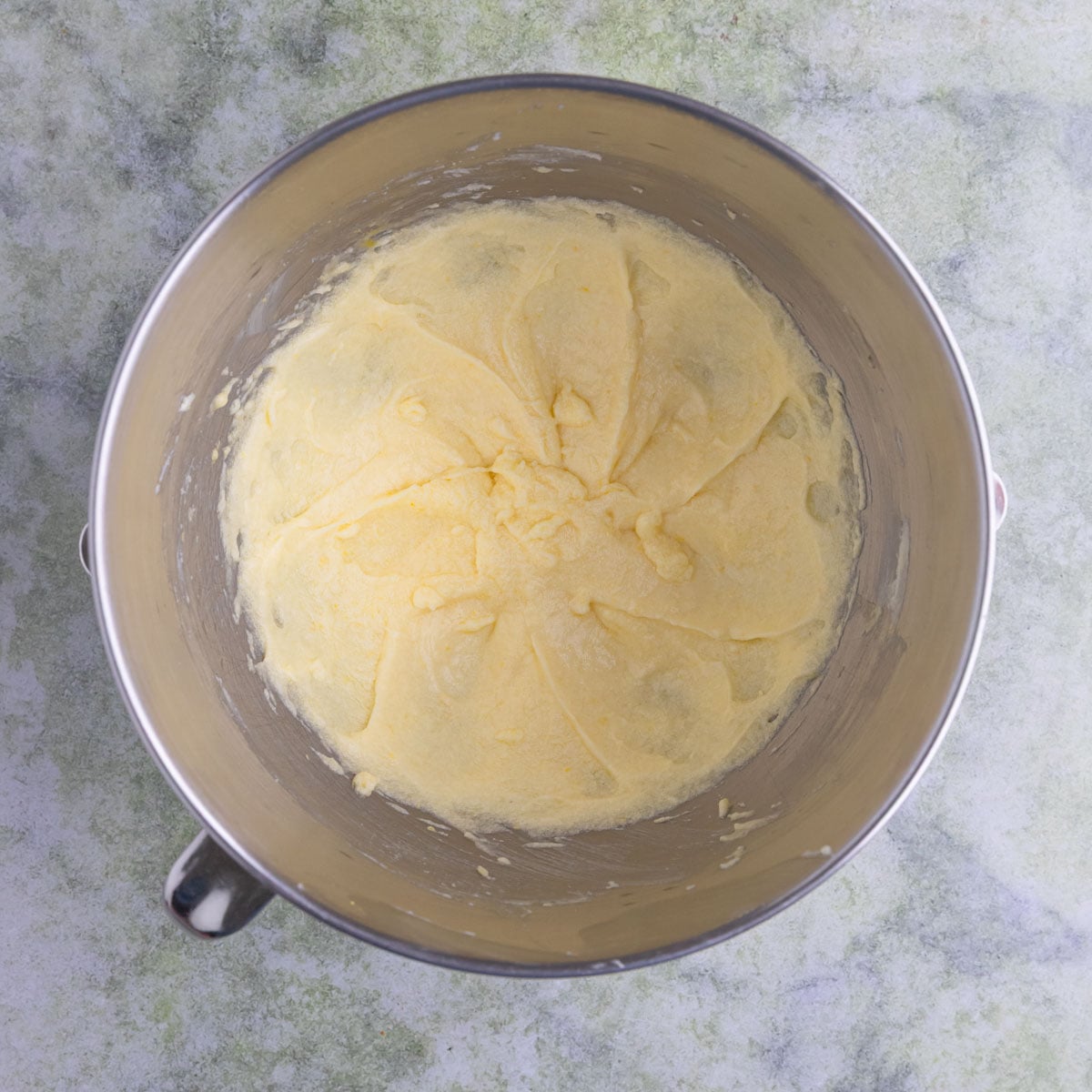 Light yelllow cake batter in the bowl of a stand mixer. The batter is creamed butter and sugar with the egg mixed in.