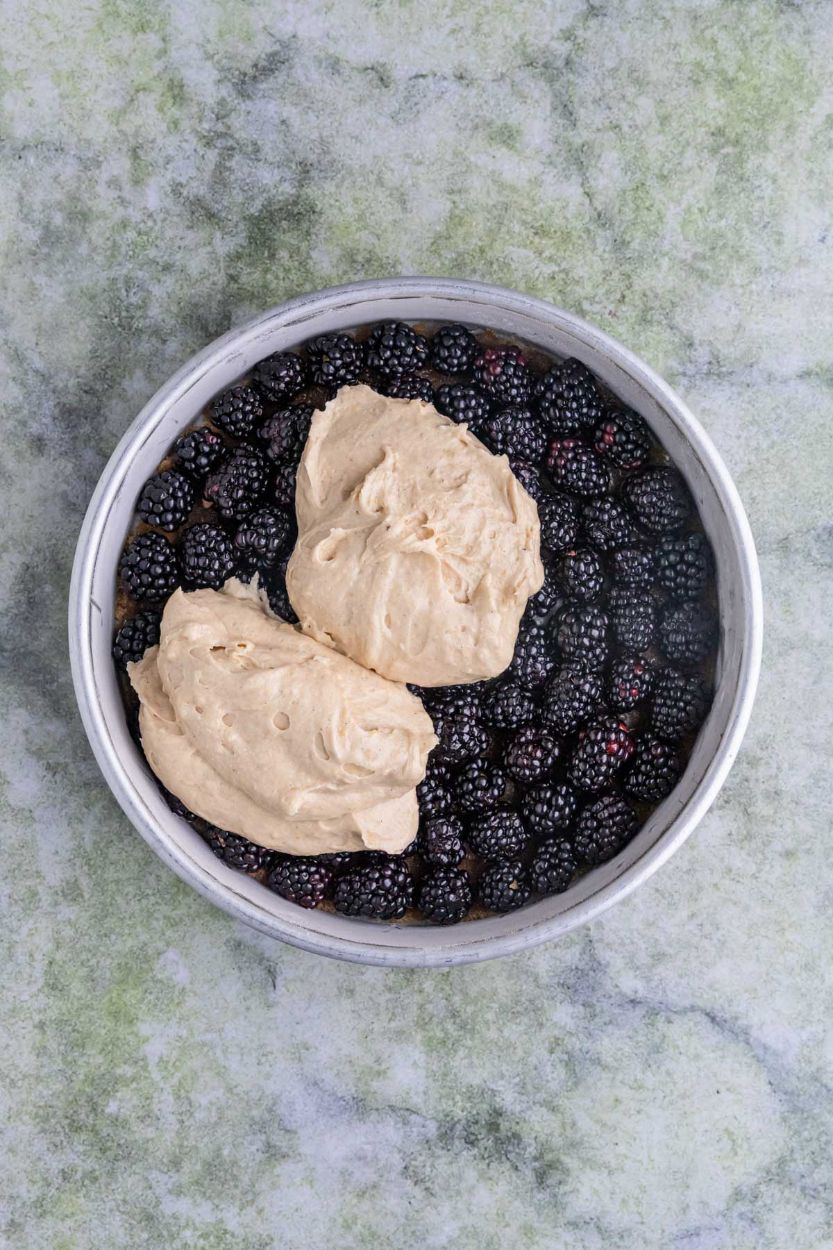 A cake pan with blackberries arranged on the bottom with two large dollops of cake batter on top.