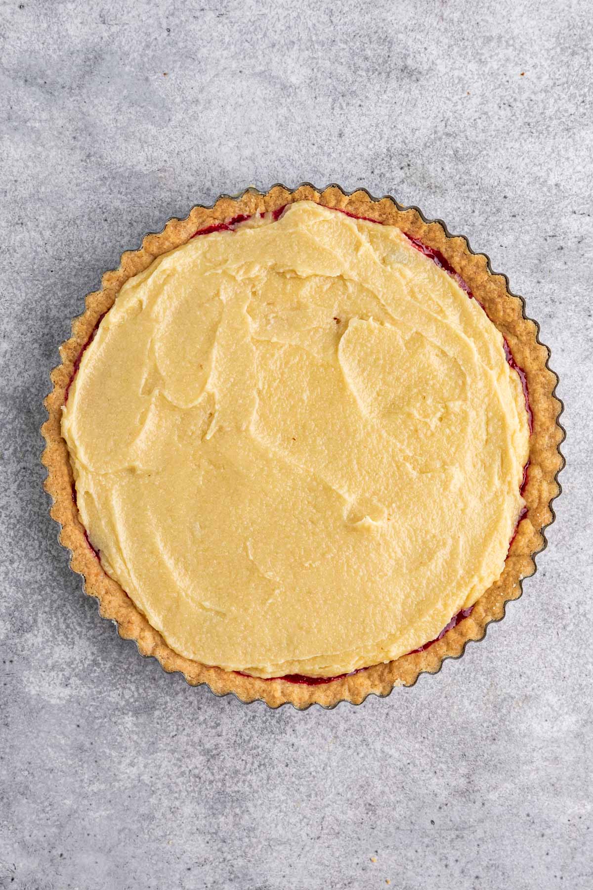 Almond frangipane filling spread of over sour cherry jam in a prebaked tart shell