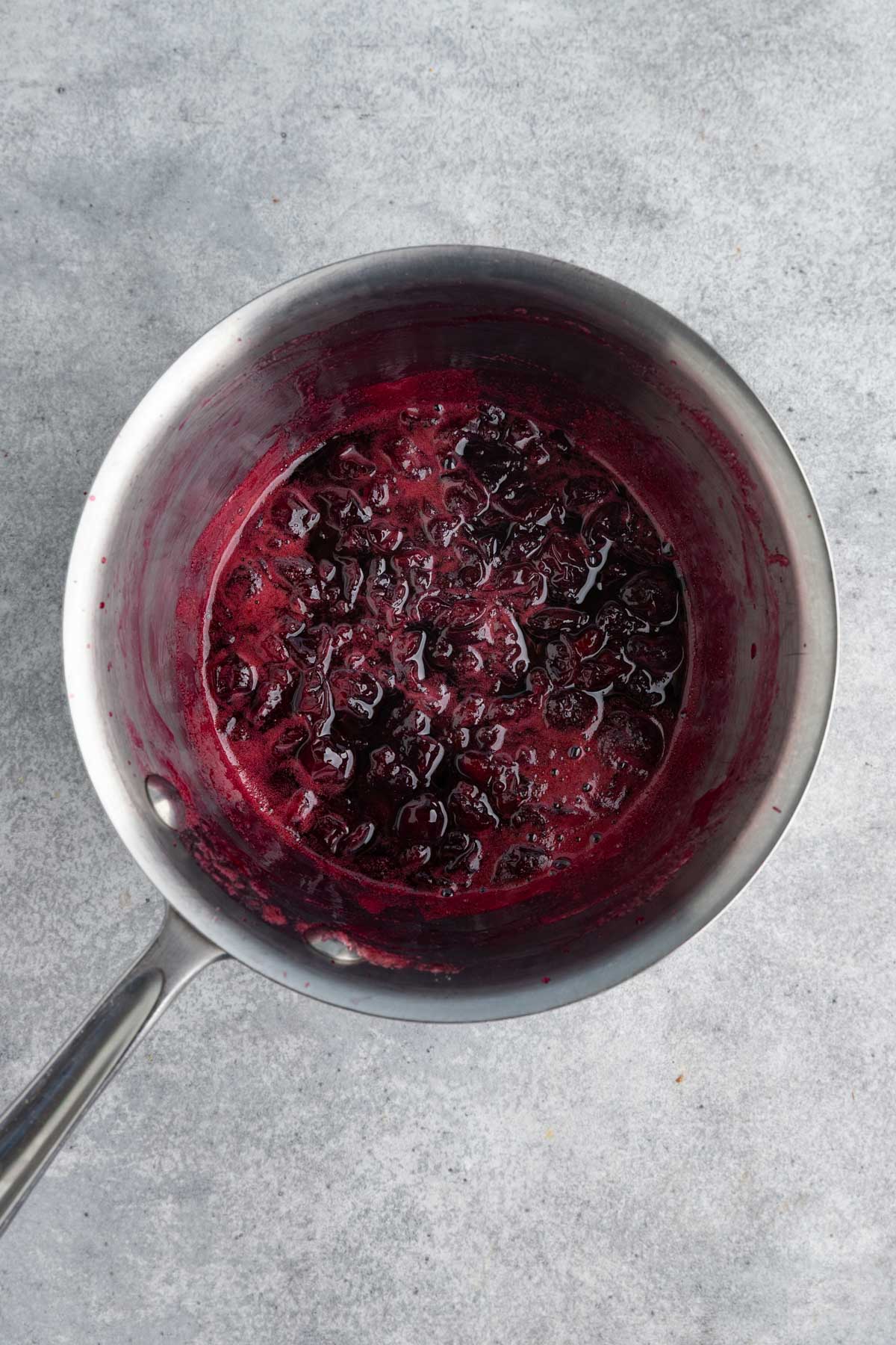 Cooked cherry jam in a stainless steel saucepan.  The cherry jam is a dark red.