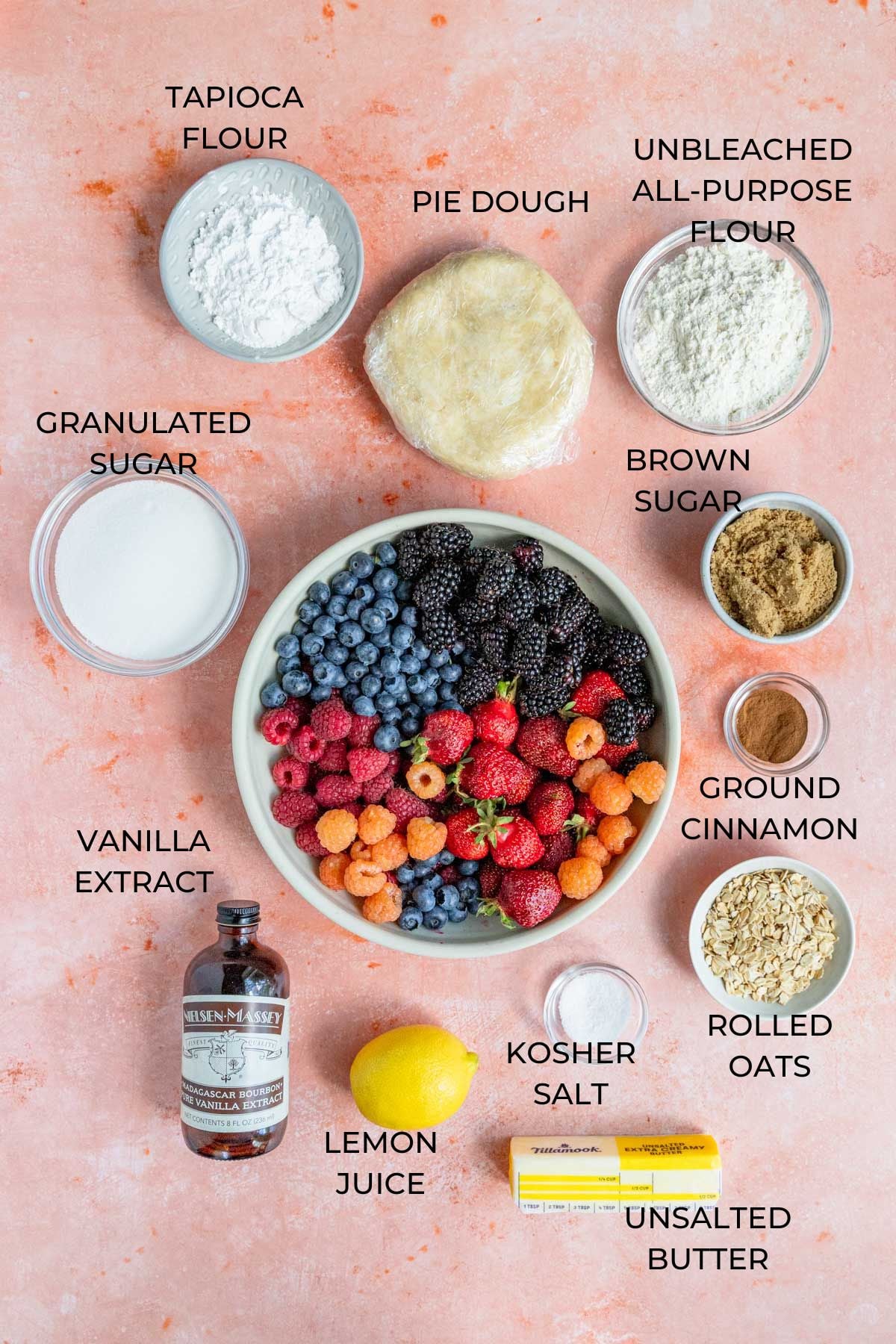 Mixed Berry Pie Ingredients - tapioca flour, pie dough, all-purpose flour, brown sugar, ground cinnamon, rolled oats, kosher salt, a lemon, vanilla extract, granulated sugar, and a large bowl of berries - blueberries, blackberries, raspberries, and strawberries