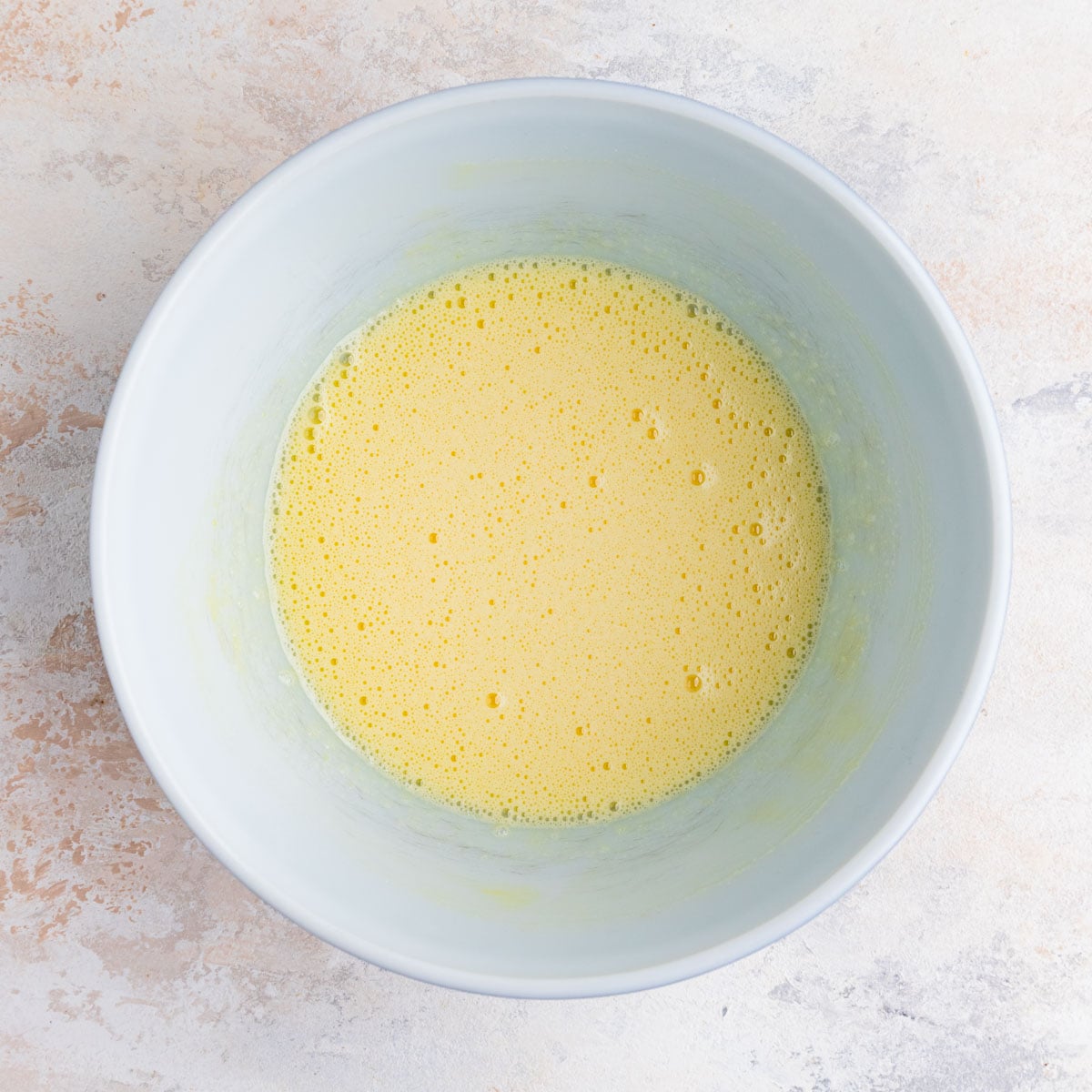Eggs and sugar whisked together in a white ceramic bowl. The mixture is light yellow