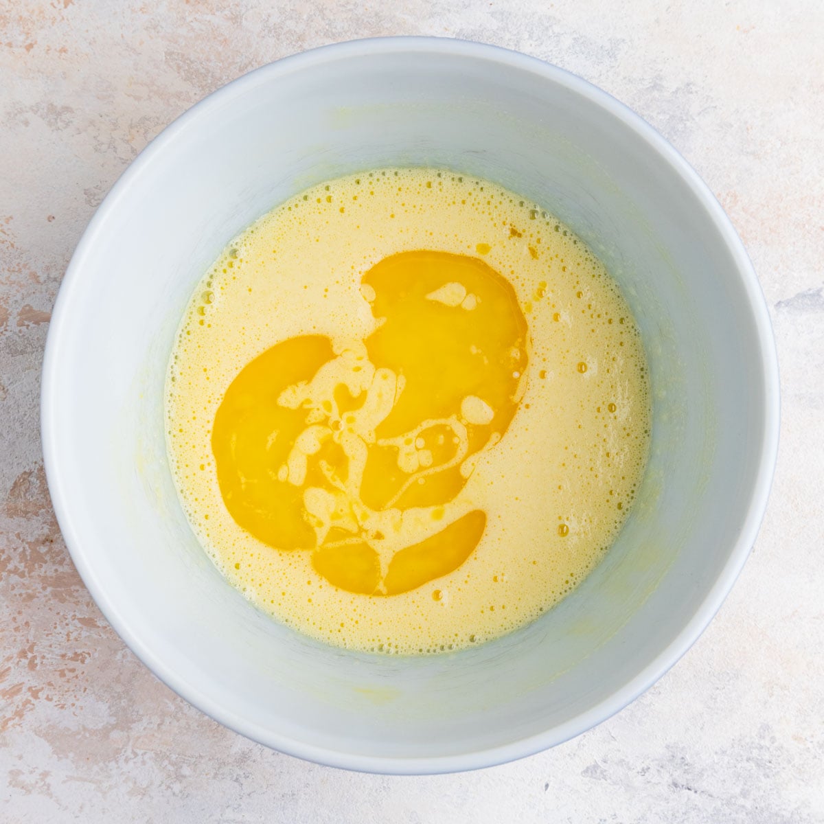 Whisked sugar and eggs with melted butter in a white ceramic bowl