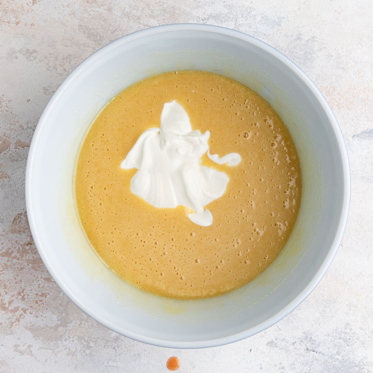 Sour cream added to the the muffin batter in a white ceramic bowl