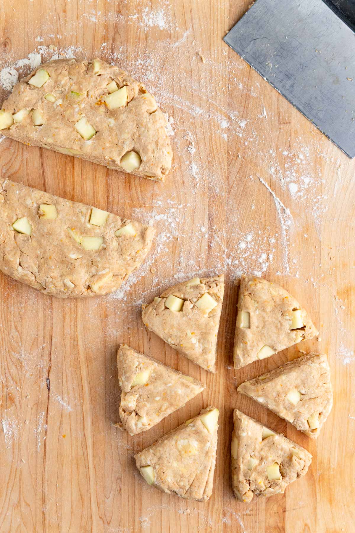 The apple scone dough on a wooden board. Once piece is cut into two pieces. The other piece is cut into 6 pieces.