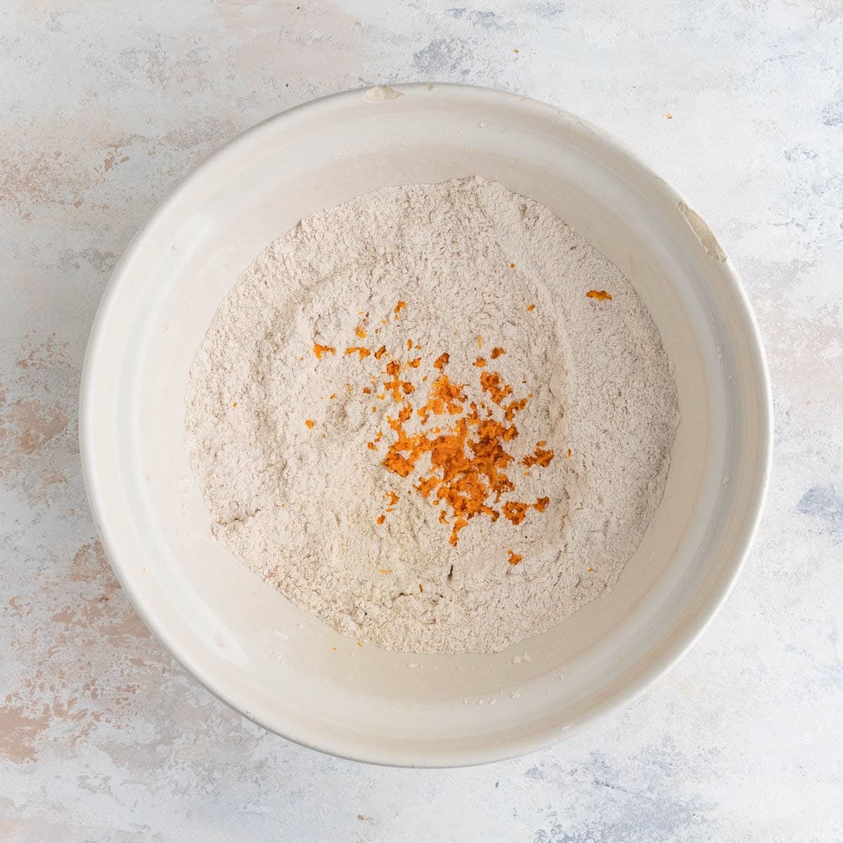 Orange zest added to the flour mixture in a white ceramic bowl. The orange zest is bright orange.