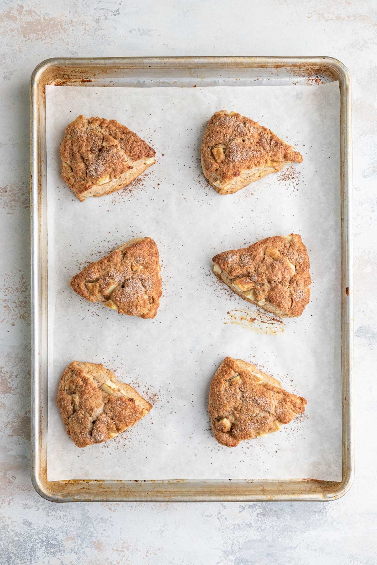 The baked scones on a parchment lined baking sheet. The scones are triangular and coated with a sugar cinnamon mixture.
