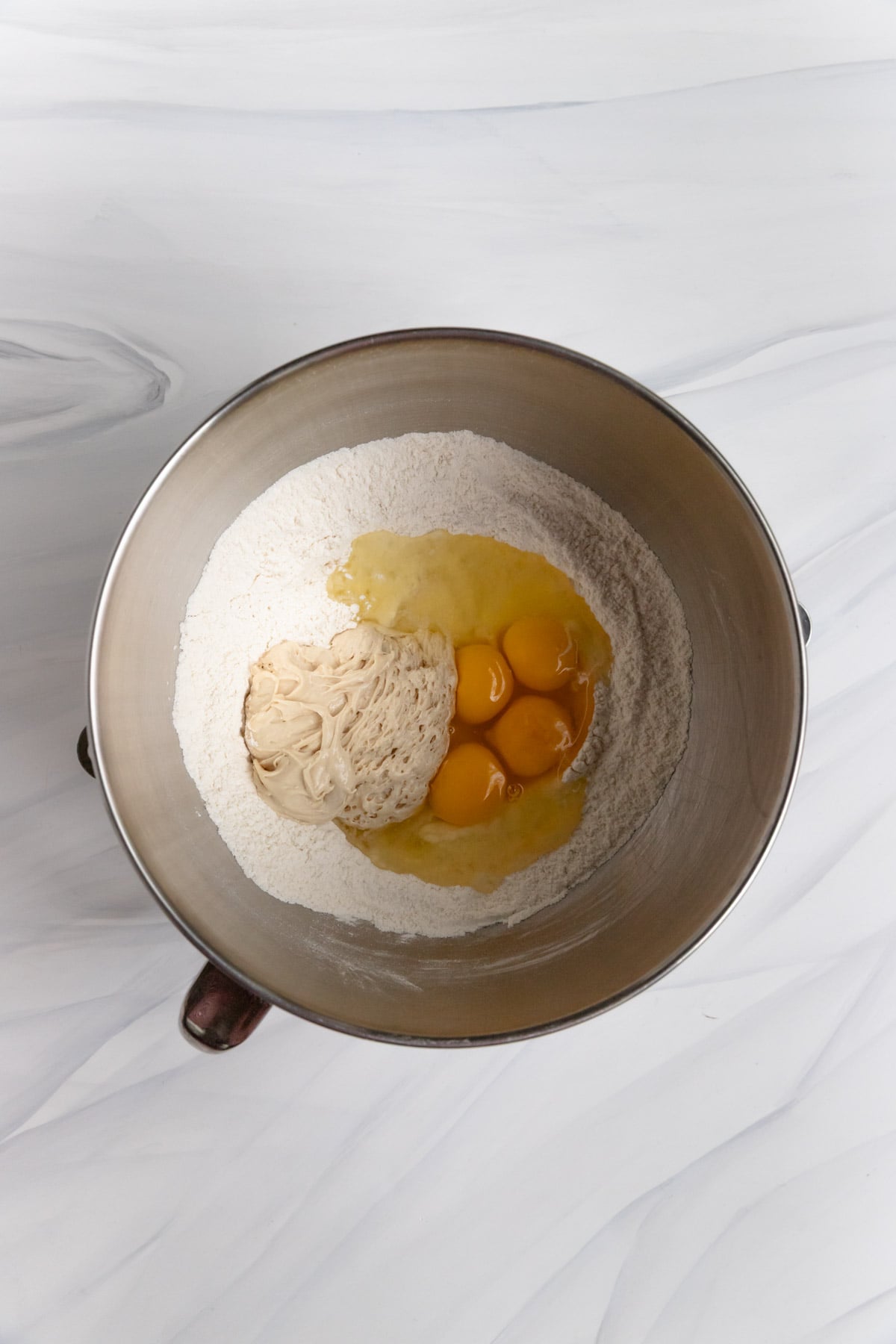 Eggs, and the preferment added to the flour sugar mixture in a metal mixing bowl.