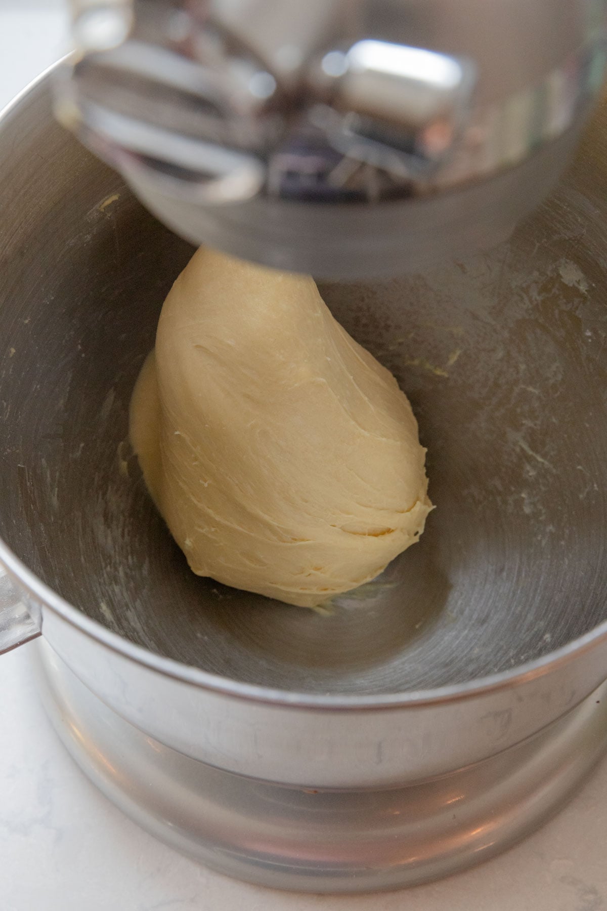The dough in a metal mixing bowl clinging to the dough hook. The dough looks smooth