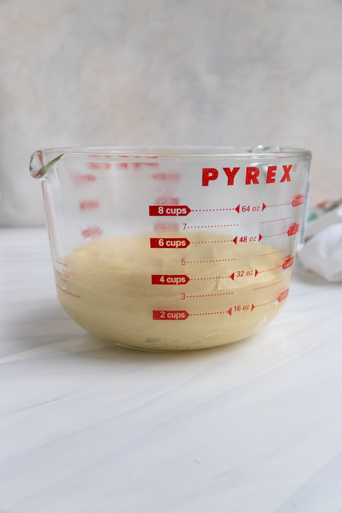A glass Pyrex measuring cup contains brioche dough, measuring just under the 4-cup line. The cup is placed on a white surface with a light background.