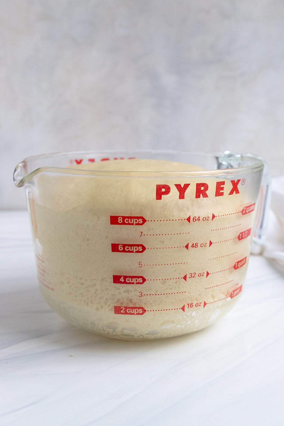 A glass Pyrex measuring cup filled with risen brioche dough up to the 8-cup mark sits on a white countertop.