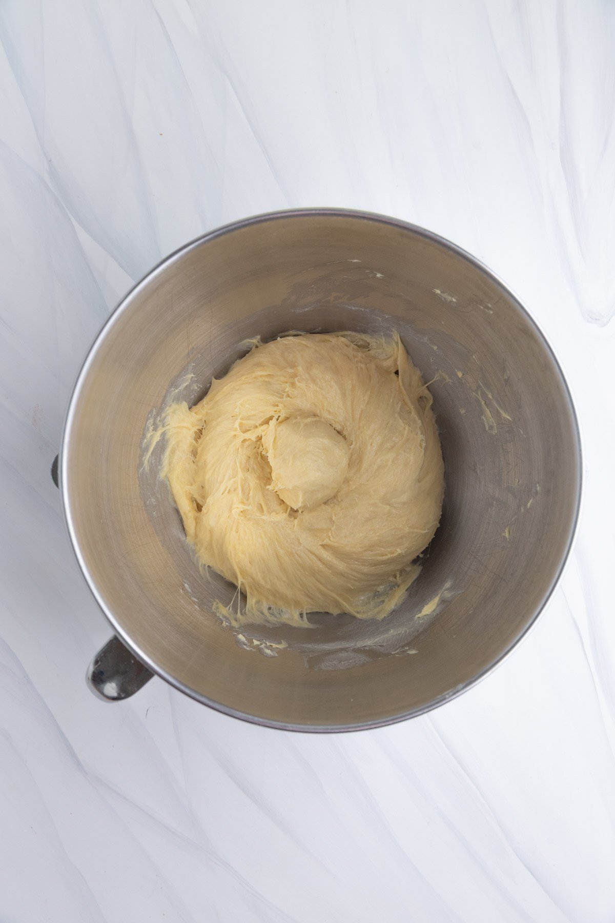 A metal mixing bowl containing a ball of brioche dough after the butter has been mixed in