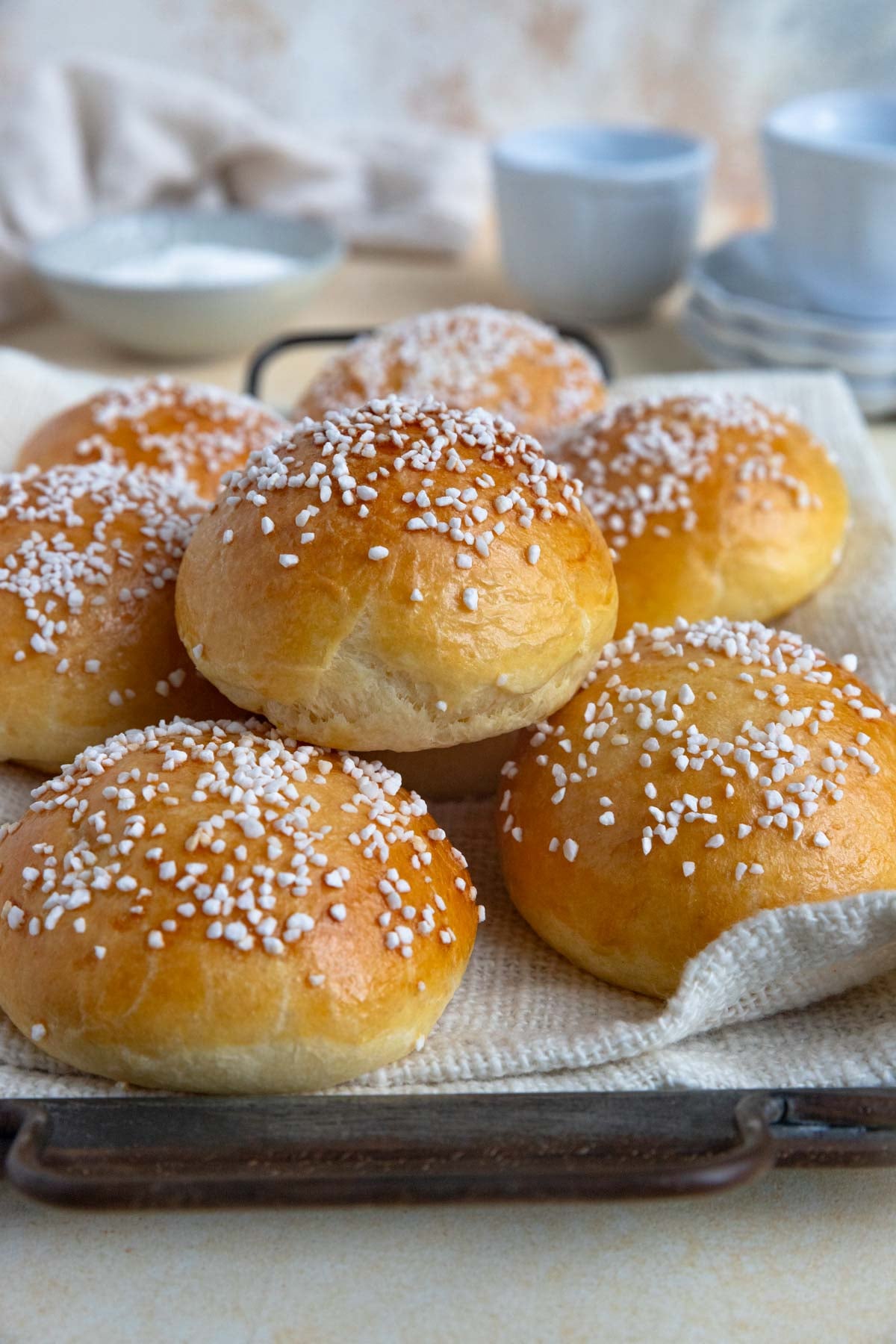 A pile of Brioche Au Sucre on a metal tray. The buns are covered with pearl sugar.