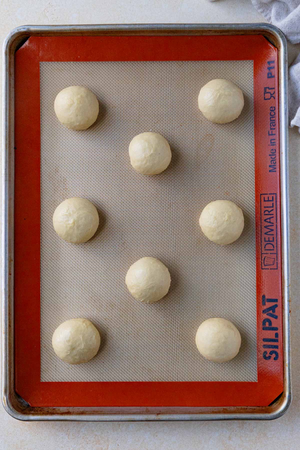 Eight pieces of dough rolled into balls arranged on a baking sheet lined with Silpat