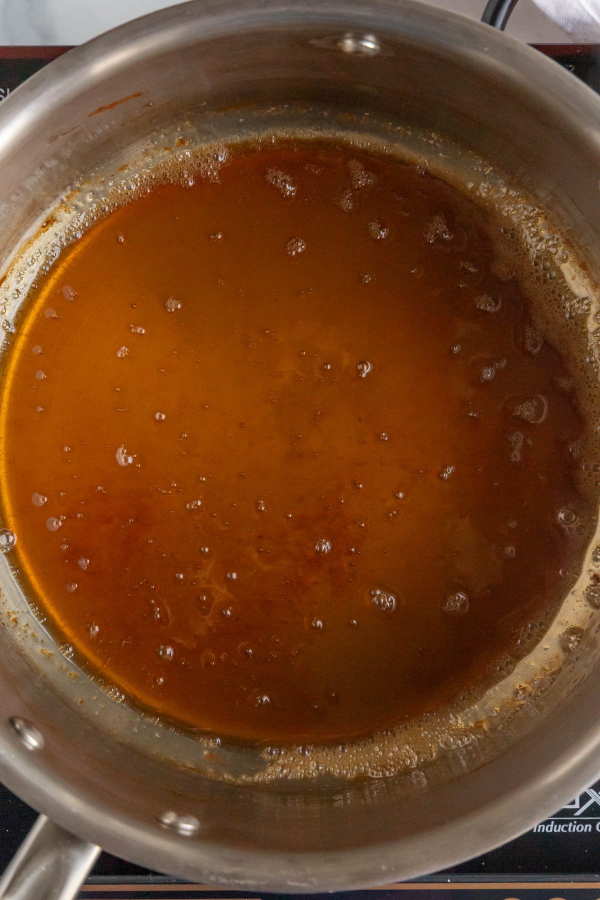A reduction of apple cider and brown sugar in a stainless steel saucepan