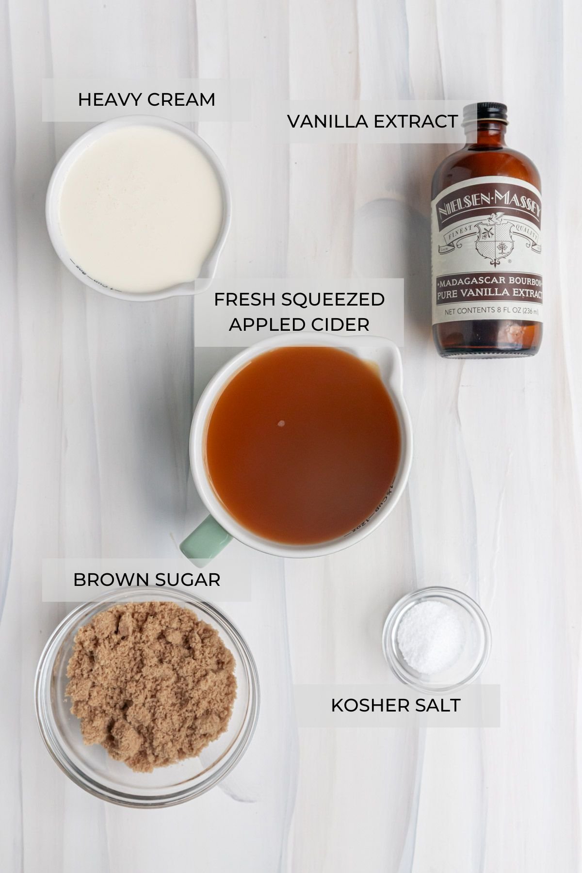 Apple cider caramel sauce ingredients arranged on a board - apple cider, heavy cream, brown sugar, kosher salt, and pure vanilla extract