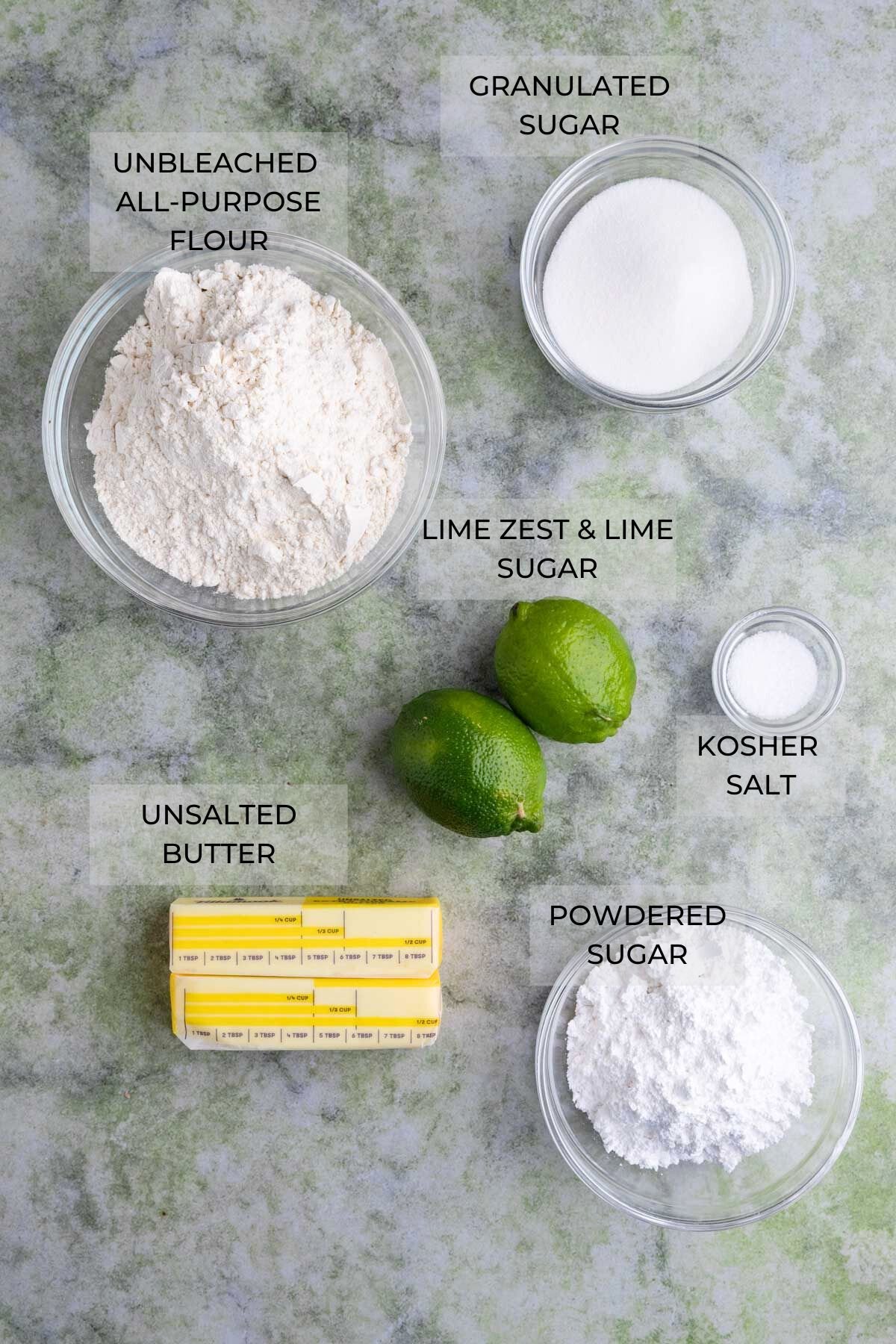 Lime shortbread cookies ingredients on a green surface - granulated sugar, kosher salt, powdered sugar, unsalted butter, fresh limes, all-purpose flour