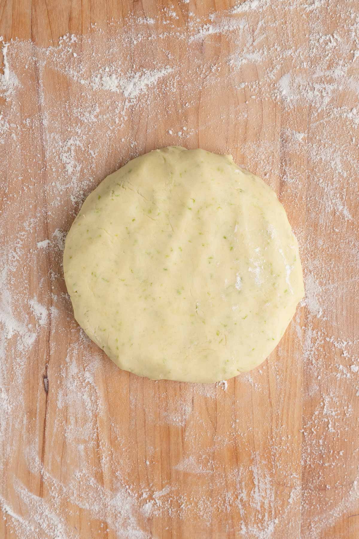 Lime shortbread cookie dough on a wooden work surface shaped into a disc