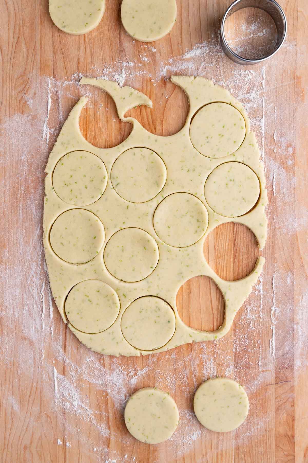 Lime shortbread cookie dough on a wooden work surface with 2-inch circles cut out of the cookie