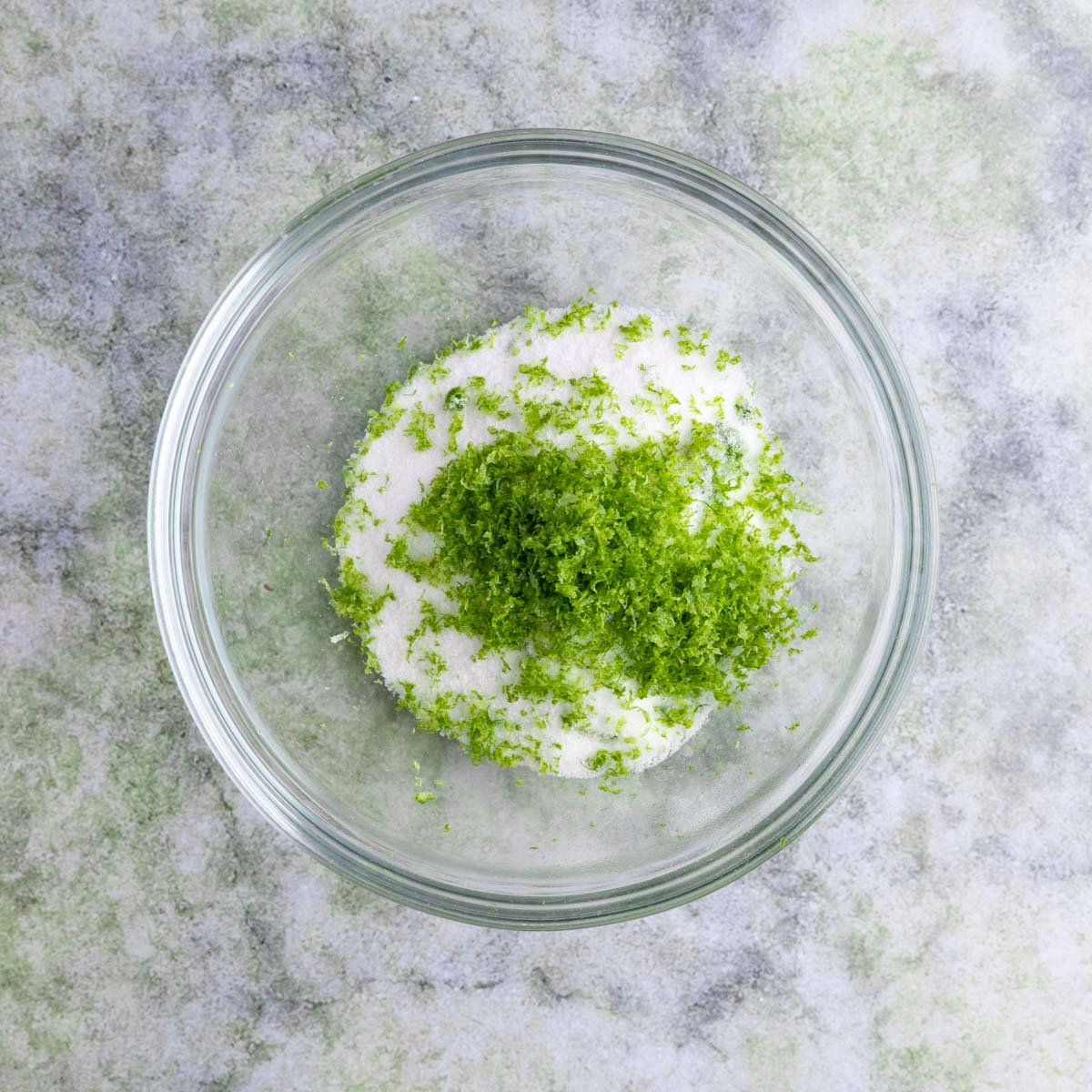 A small glass bowl filled with sugar and lots of lime zest