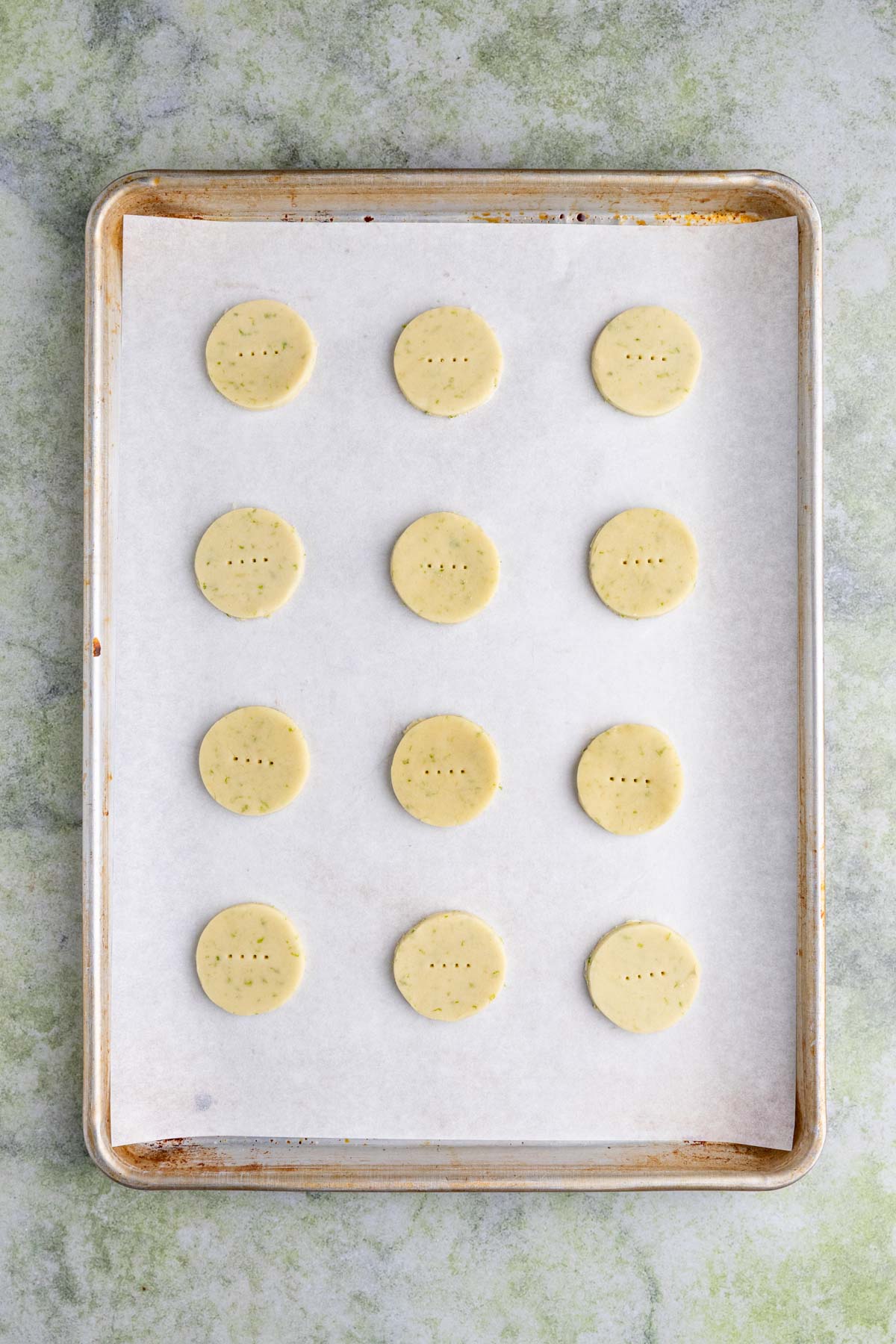 Twelve unbaked lime shortbread cookies on a parchment lined baking sheet