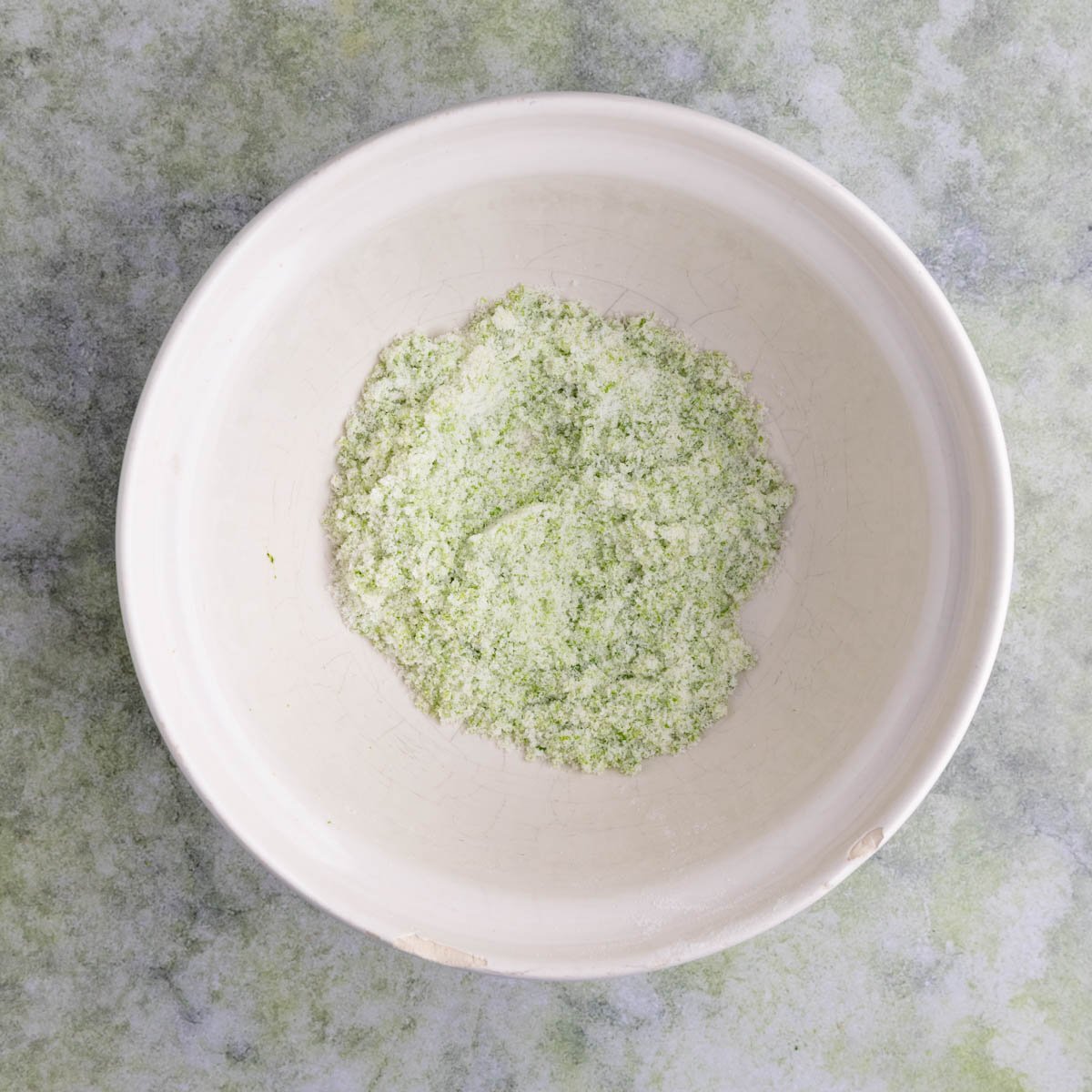 The lime sugar mixture in a ceramic mixing bowl.  The sugar looks green