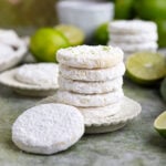 Two small stacks of lime shortbread cookies on two small plates with a teacup and small limes in the background.