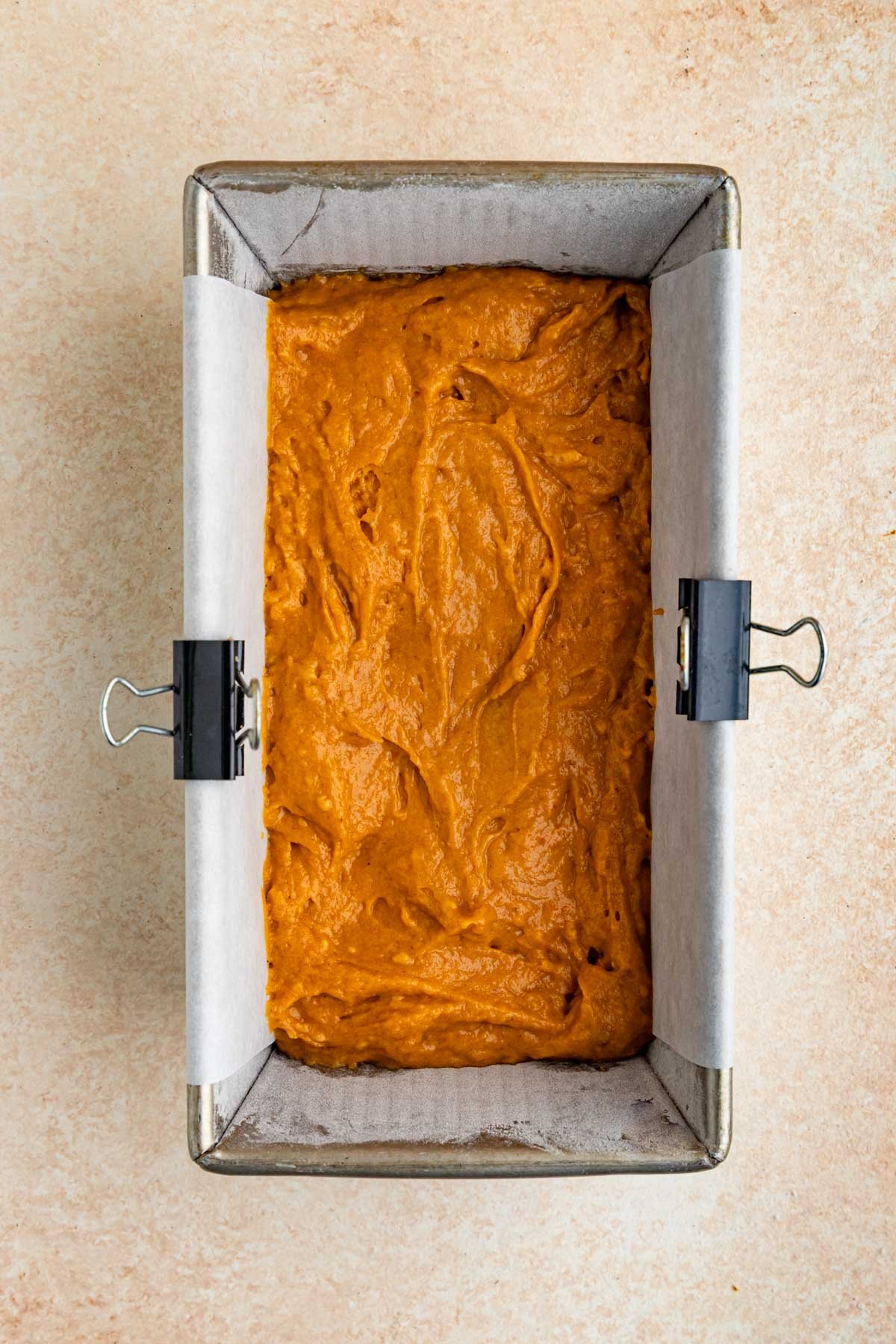An 8.5 x 4.5-inch loaf pan filled half way with pumpkin bread batter. The batter is a burnt orange color