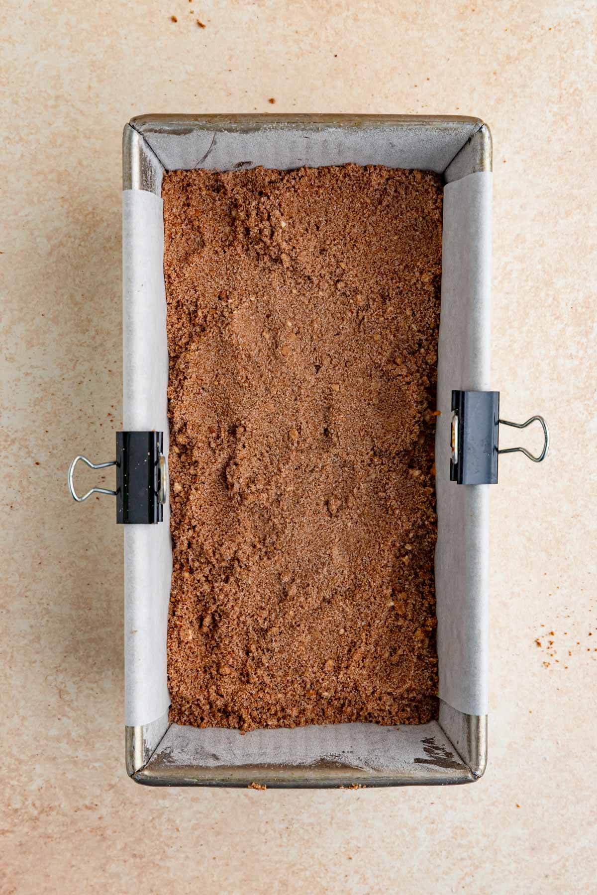An 8.5 x 4.5-inch loaf pan filled half way with pumpkin bread batter. The batter is topped with a sugar-cinnamon-pecan mixture