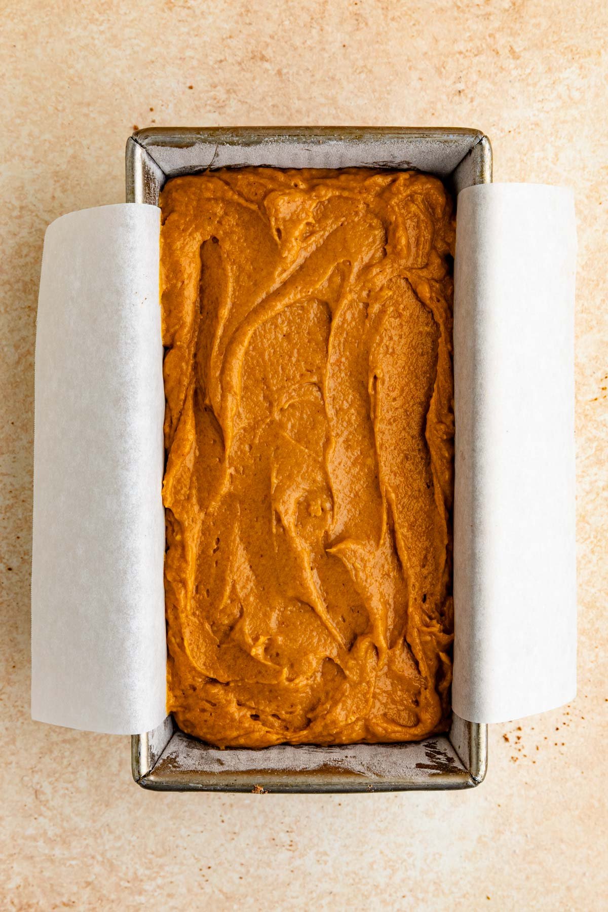 An 8.5 x 4.5-inch loaf pan filled with pumpkin bread batter. The batter is a burnt orange color.