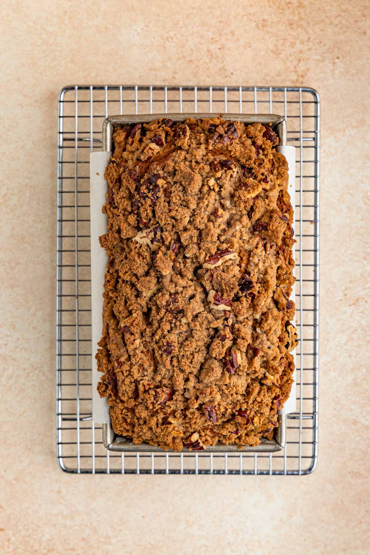 Baked pumpkin bread with pecan streusel topping in an 8.5 x 4.5-inch loaf pan. The pan is sitting on top of a wire rack.