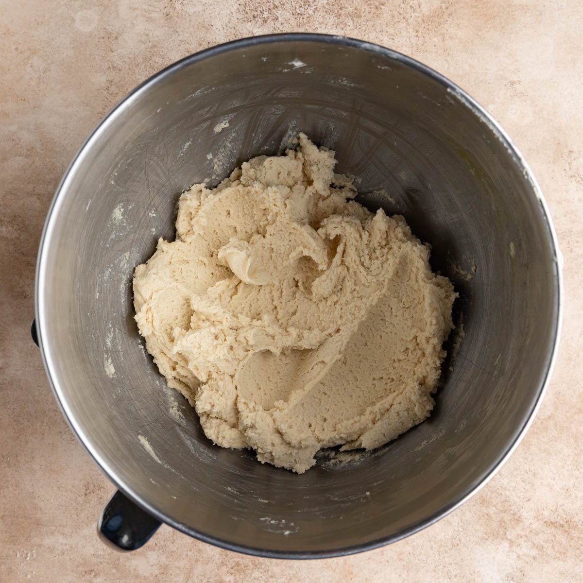 The cookie dough in the bowl of a stainless steel mixer. The dough is a light beige color