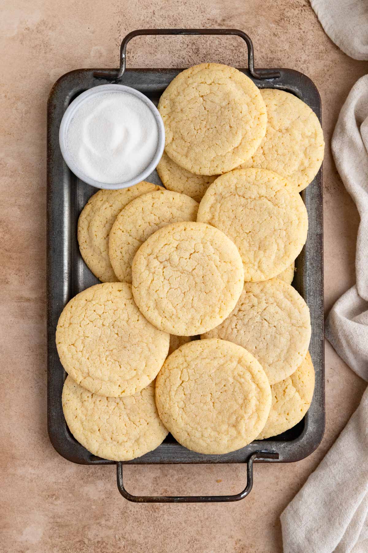 Several vanilla sugar cookies arranged on a dark gray platter with a small bowl of sugar in the upper left hand corner