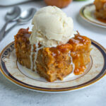 A serving of apple bread pudding on a small plate with a large scoop of vanilla ice cream