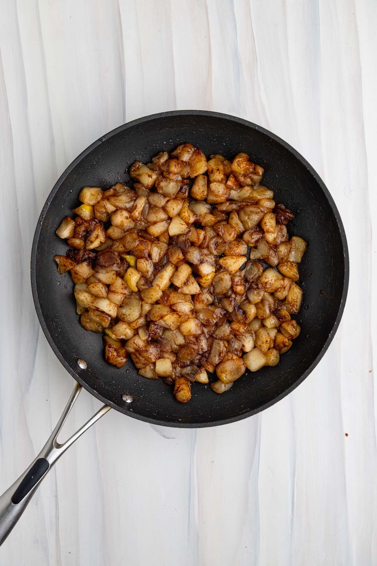 Caramelized apples in a nonstick pan. The apples are dark brown from caramelized and cinnamon