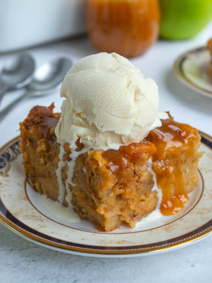 A serving of apple bread pudding on a small plate with a large scoop of vanilla ice cream