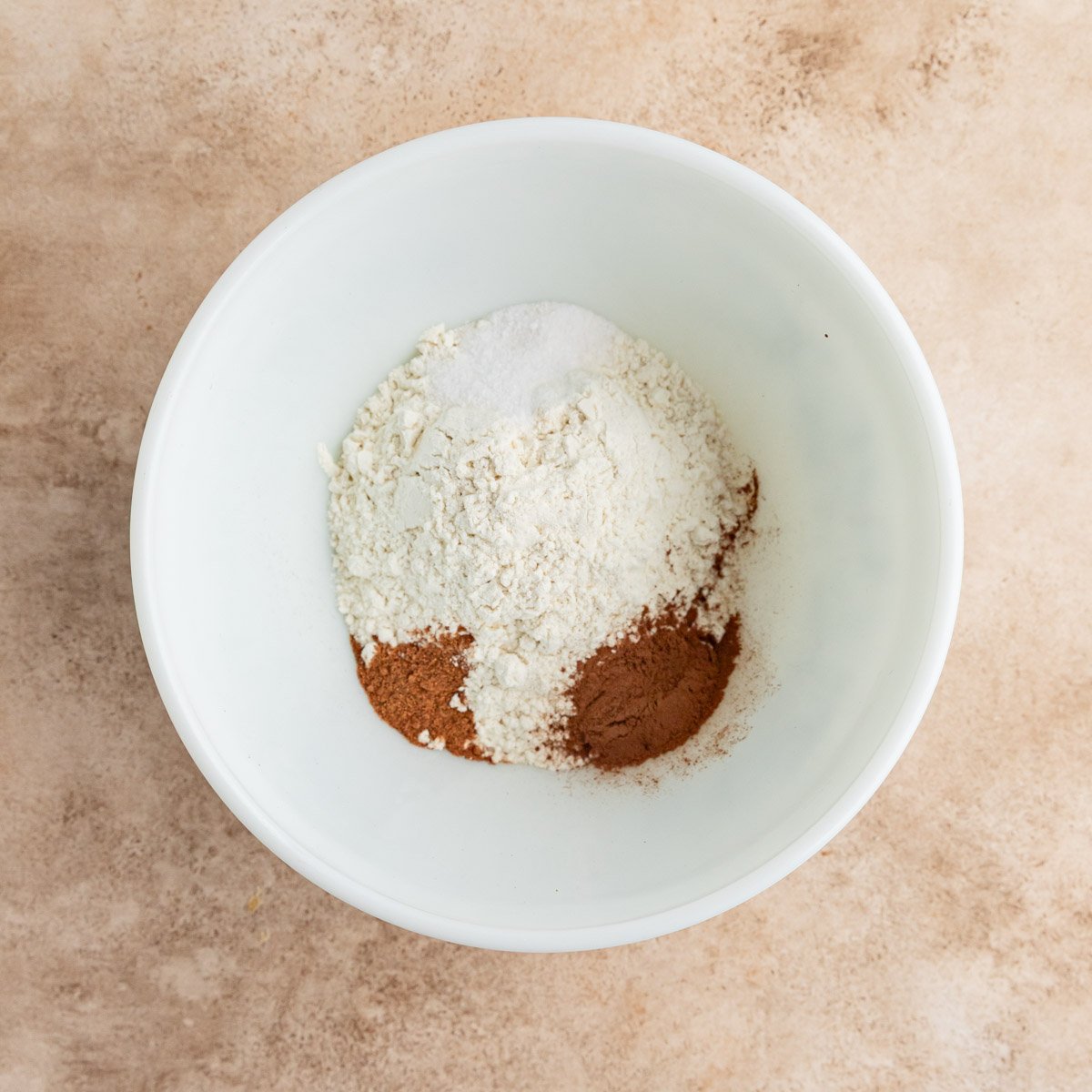 Ap flour, salt, ground nutmeg, ground cinnamon in a white ceramic bowl
