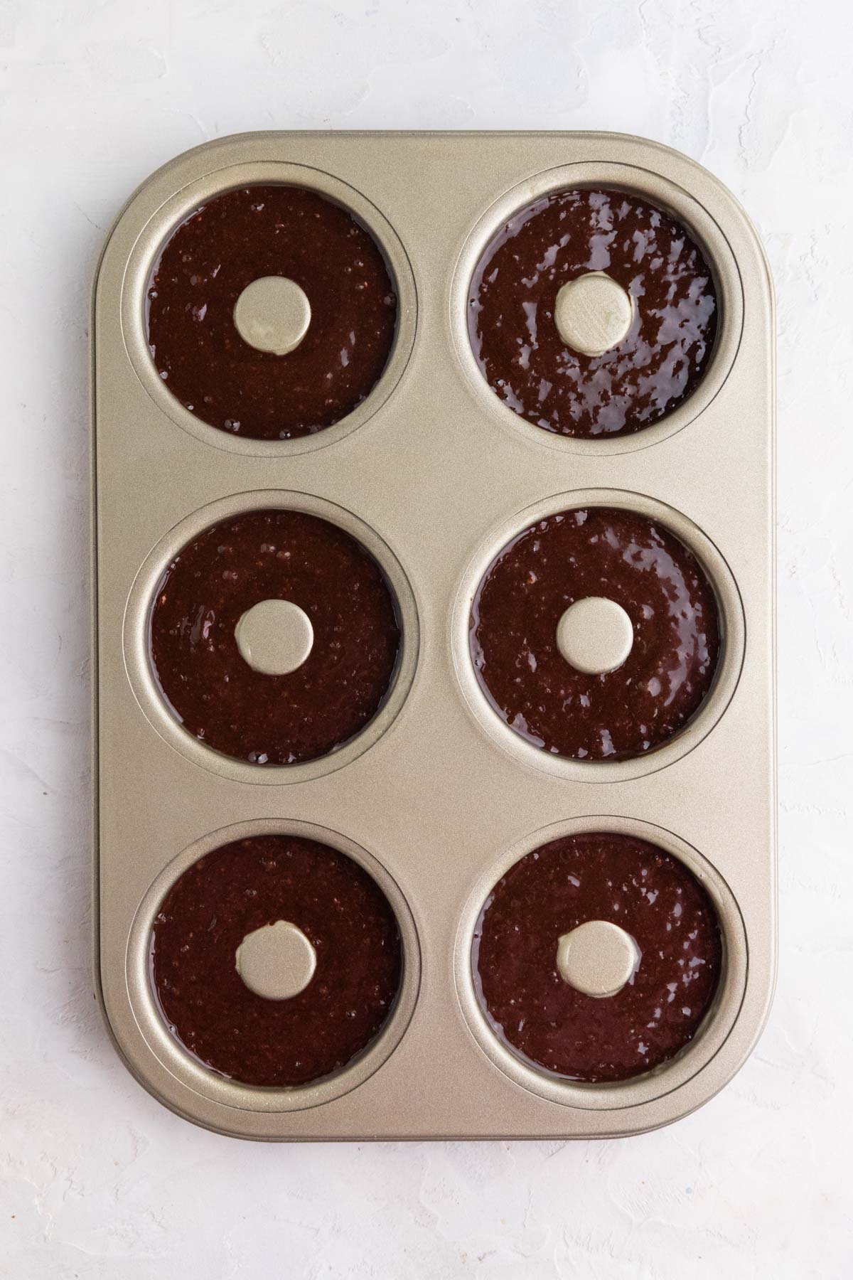 A 6 well doughnut pan with chocolate doughnut batter in each well