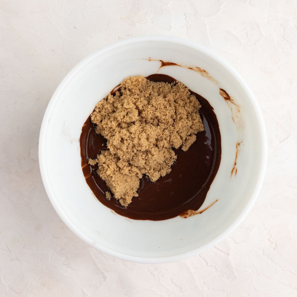 Brown sugar sitting on top of a chocolate paste and egg mixture in a white ceramic bowl