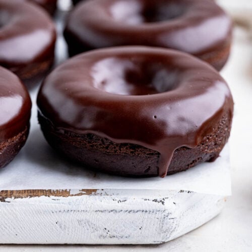Chocolate doughnuts with a chocolate glaze on a white wooden board lined with parchment paper