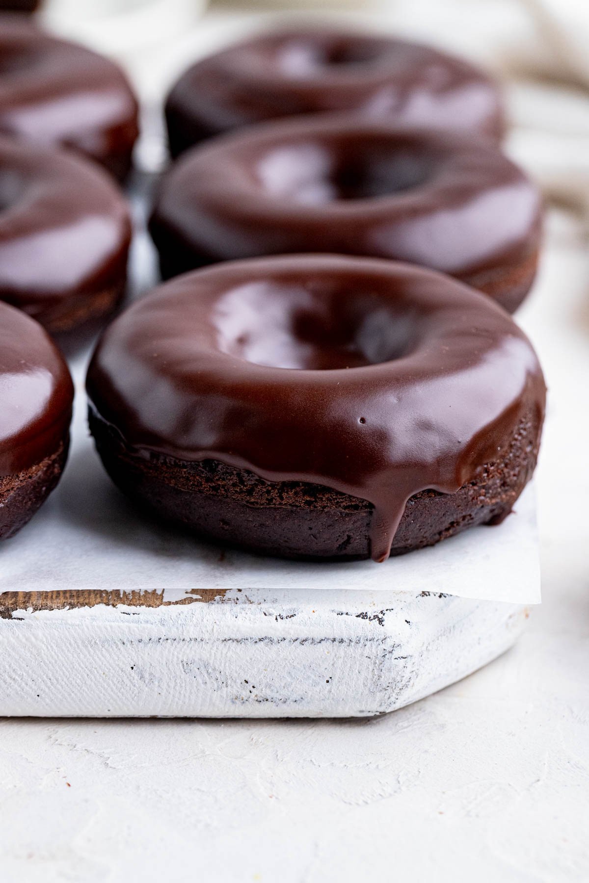 Chocolate doughnuts with a chocolate glaze on a white wooden board lined with parchment paper