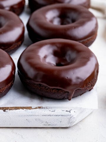 Chocolate doughnuts with a chocolate glaze on a white wooden board lined with parchment paper