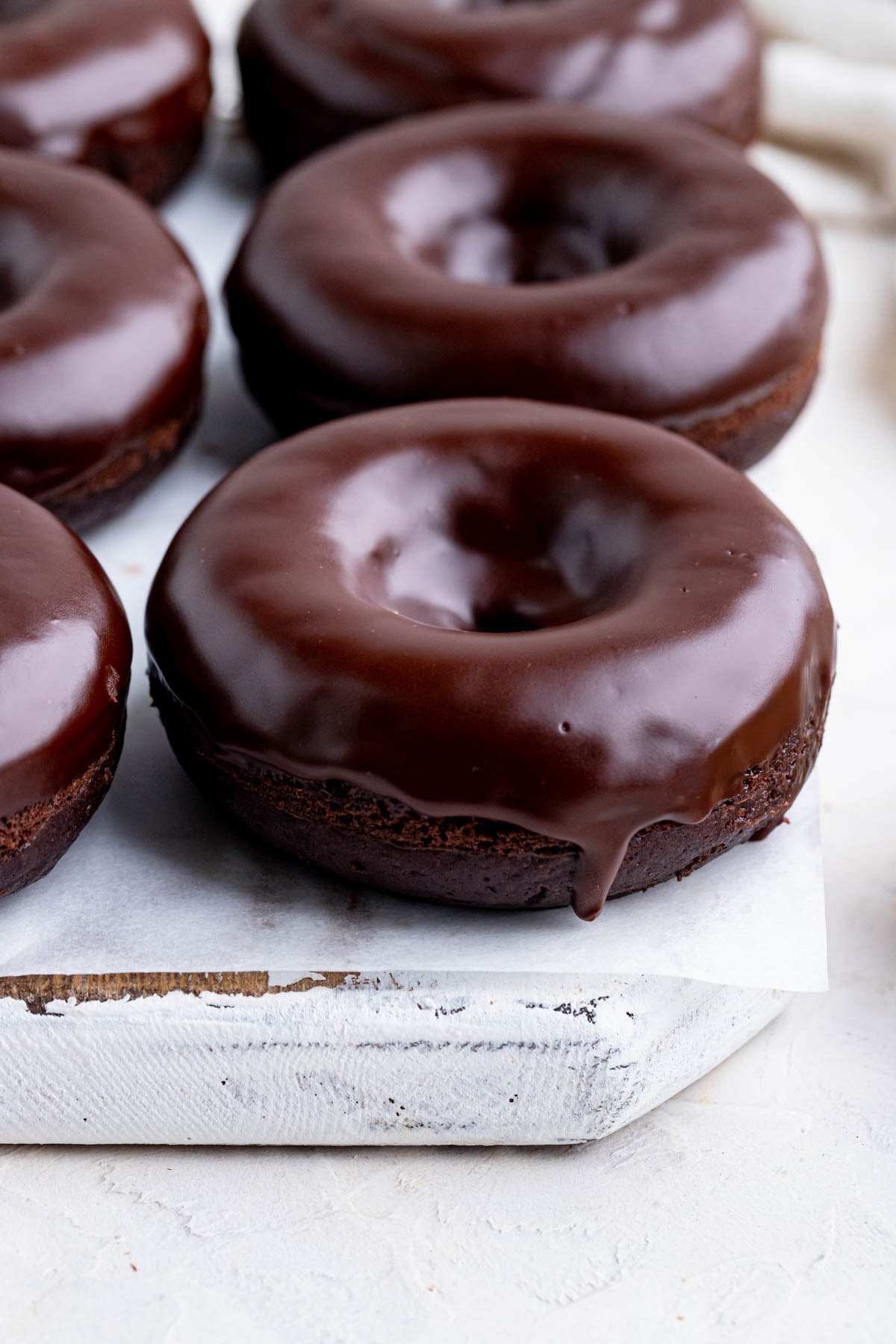 Chocolate doughnuts with a chocolate glaze on a white wooden board lined with parchment paper