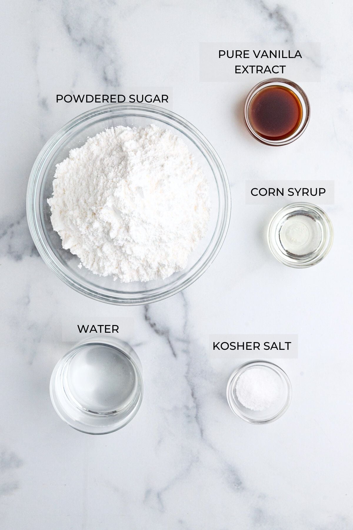 Cookie icing ingredients arranged on a board - powdered sugar, vanilla extract, corn syrup, kosher salt, water