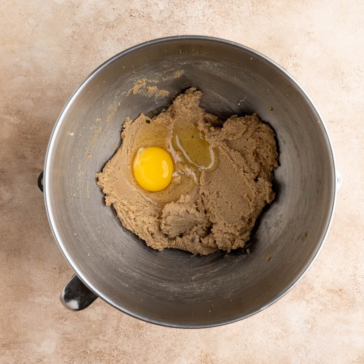 Creamed butter and sugar in a mixing bowl. The sugar butter mixture is brown and looks creamy. There is a whole egg on top of the sugar butter mixture