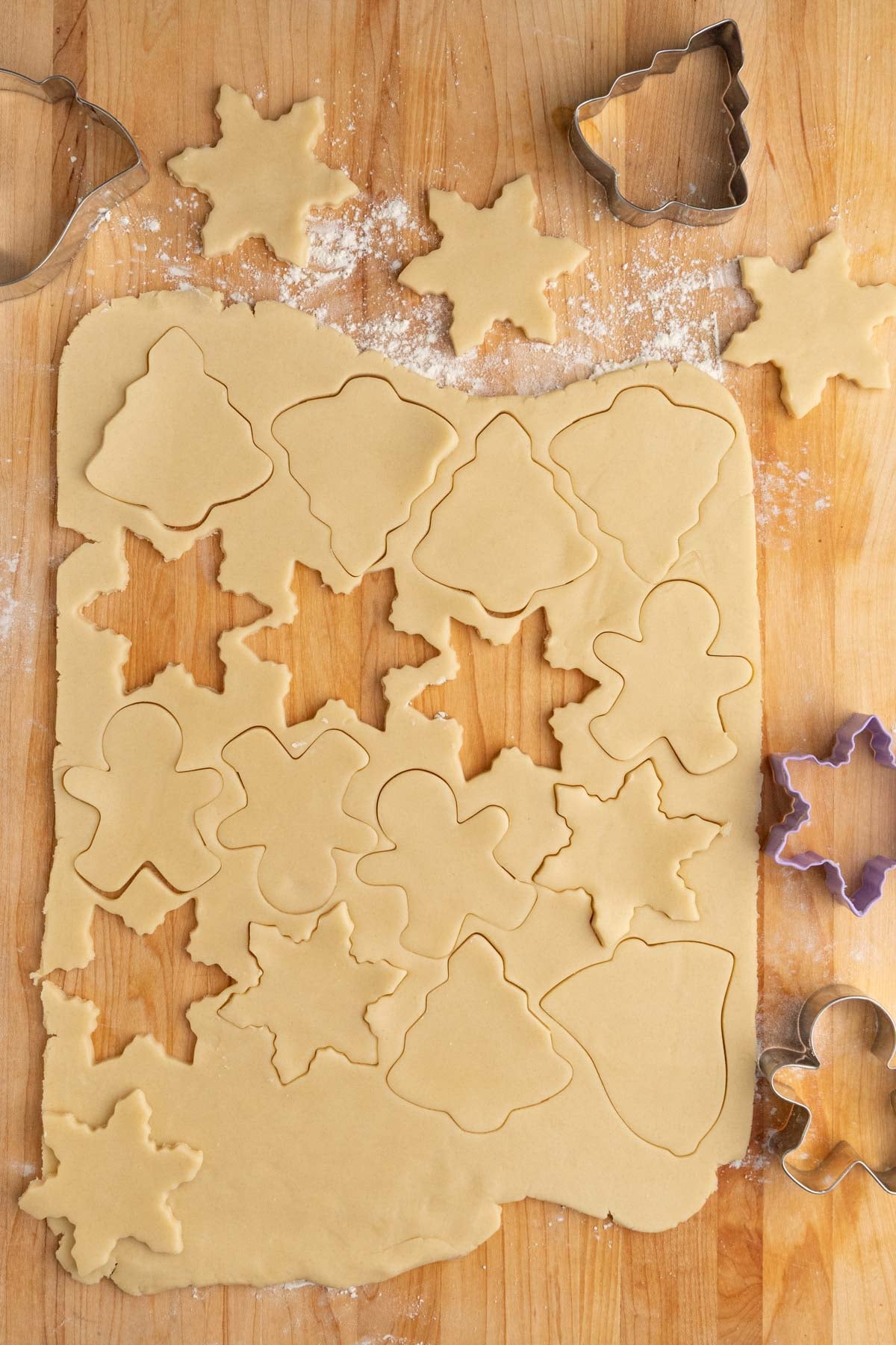 Shortbread cookie dough rolled out on a wooden work surface with several shapes cut out with Christmas cookie cutters