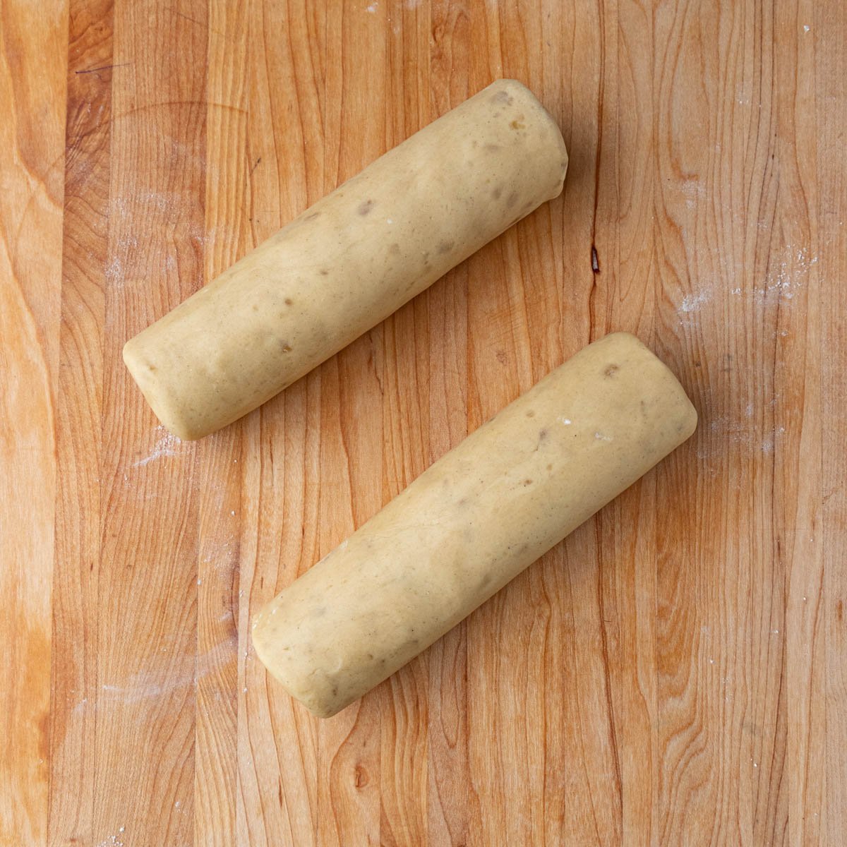 Ginger shortbread cookie dough shaped into 2 dough logs. The dough logs are on a wooden board.