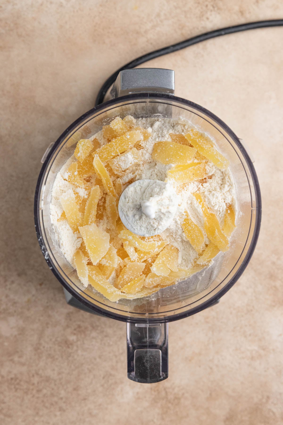 Pieces of chopped crystallized ginger and flour in the bowl of a mini food processor