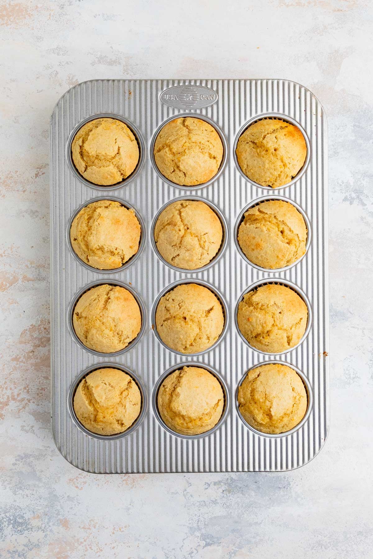 12 baked orange muffins in a silver muffin pan